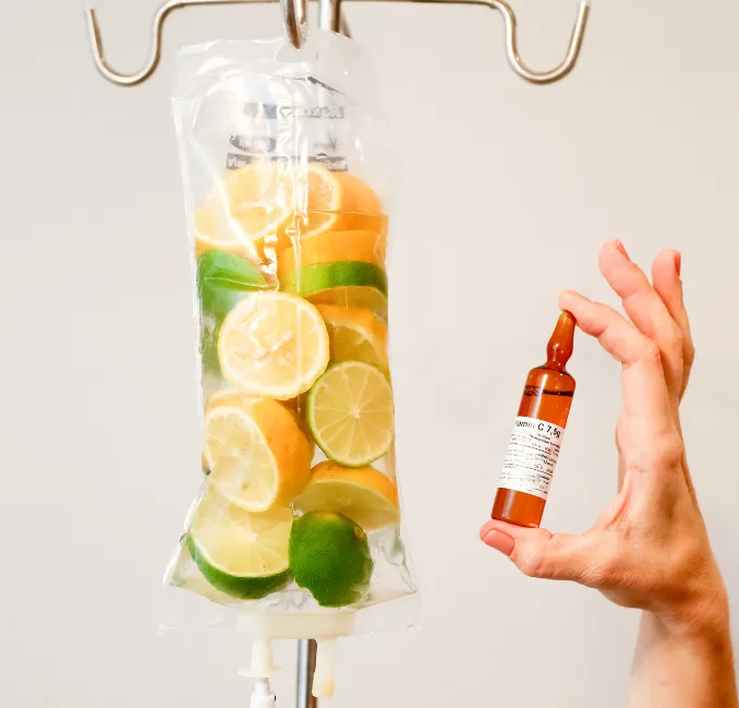 IV drip bag filled with lemon and lime slices, next to a hand holding a small amber glass vial