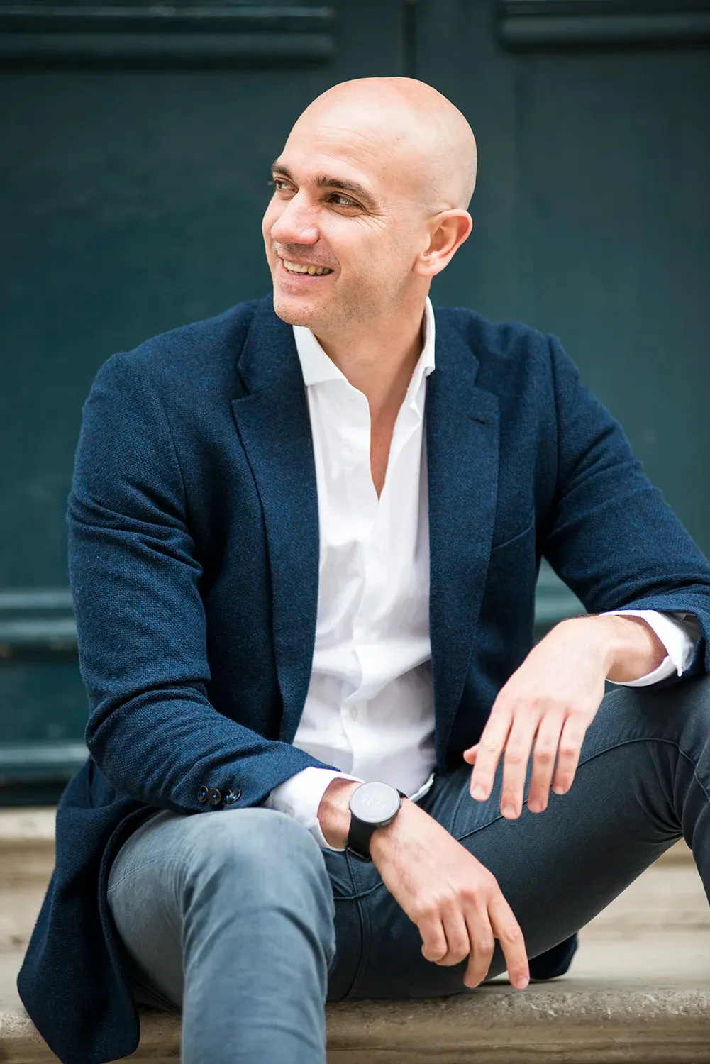 Man in a navy blazer and white shirt smiling, sitting on stone steps
