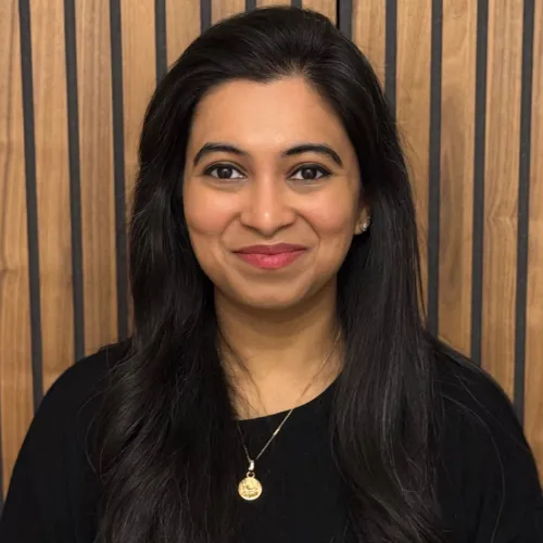 Dr Gunjan Modi smiling, in a black top, in front of a wooden slatted wall