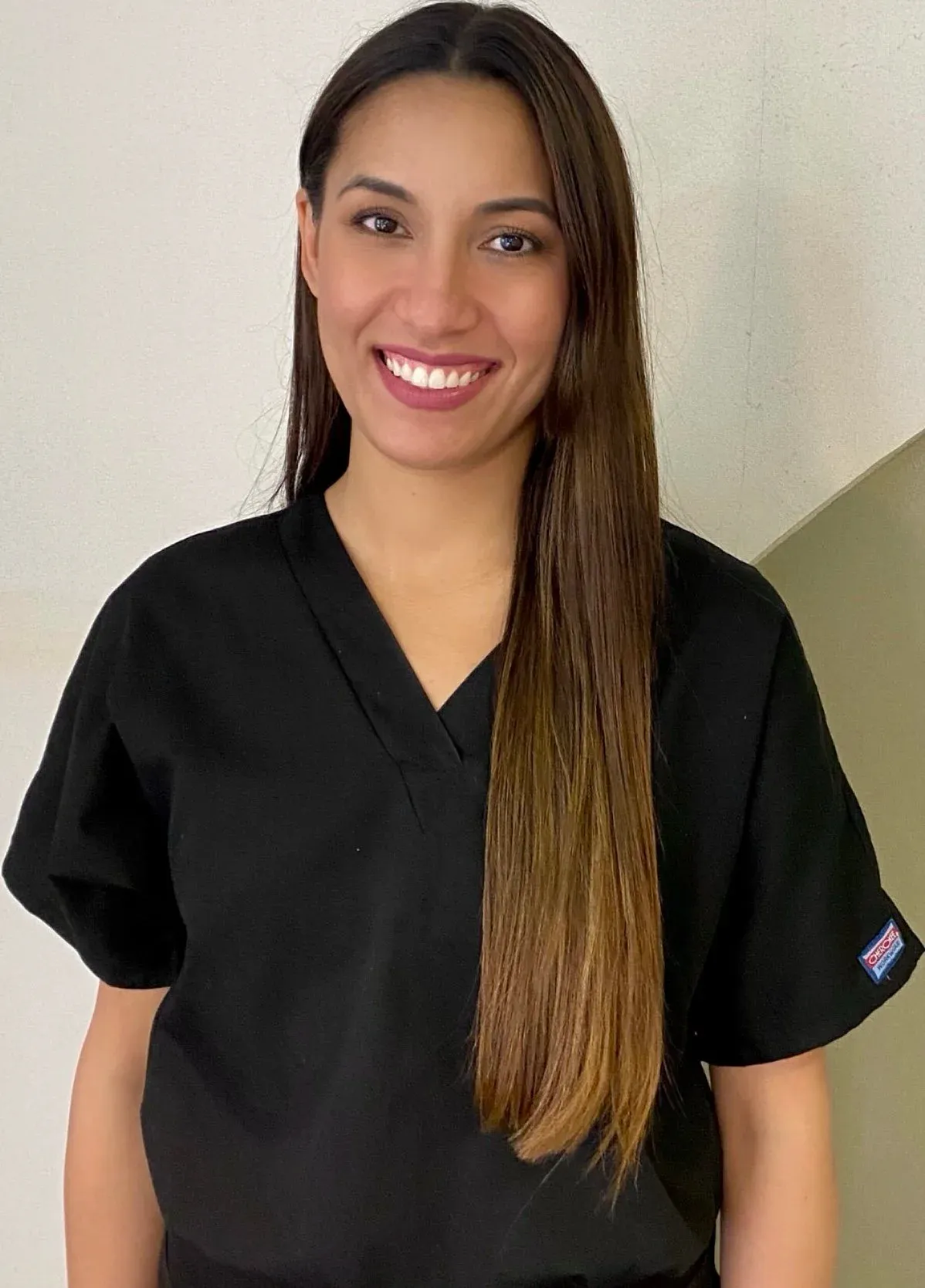 Woman with long dark hair smiling, in black scrubs