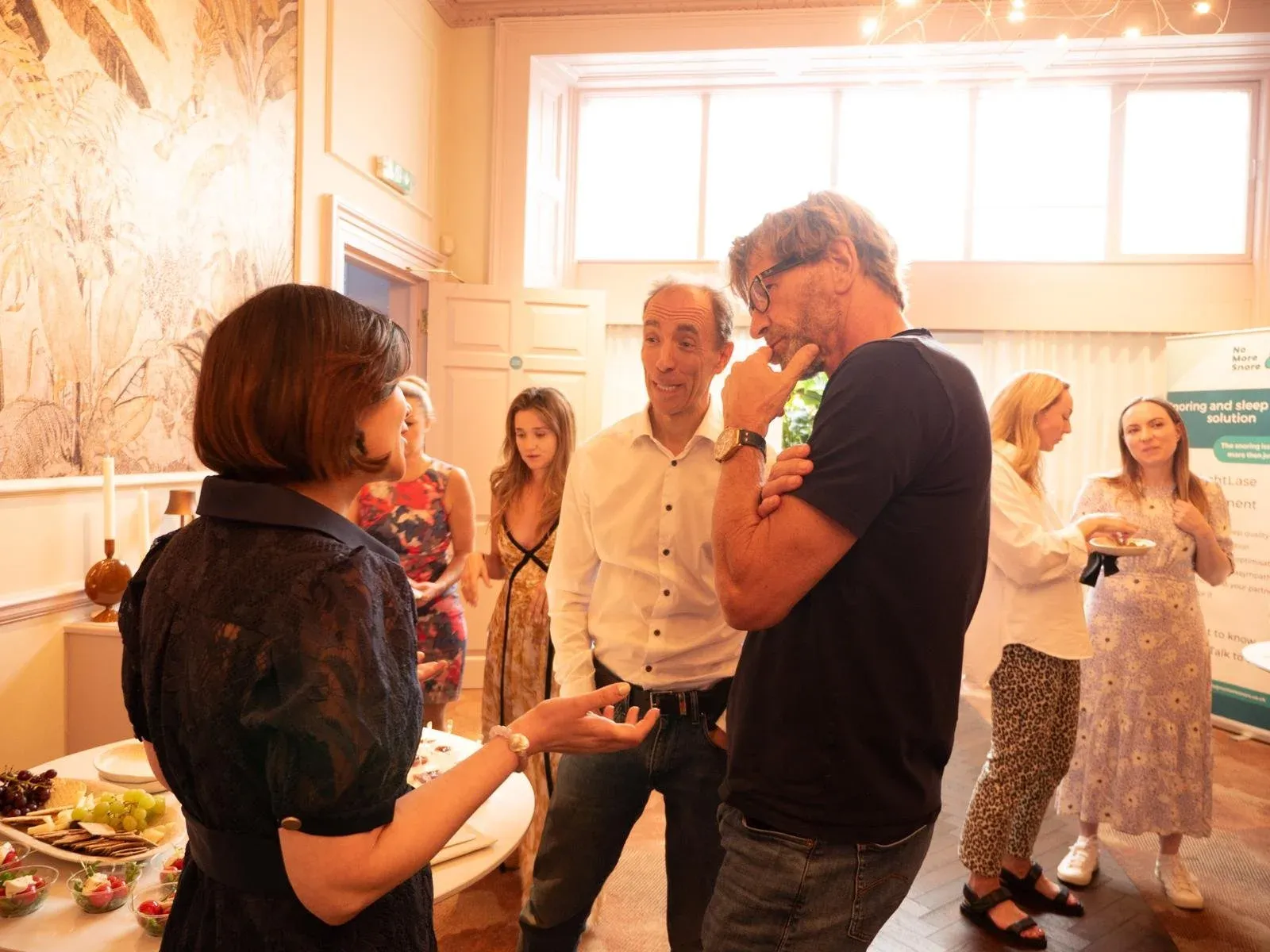 Guests standing and talking around a table of food at an evening event