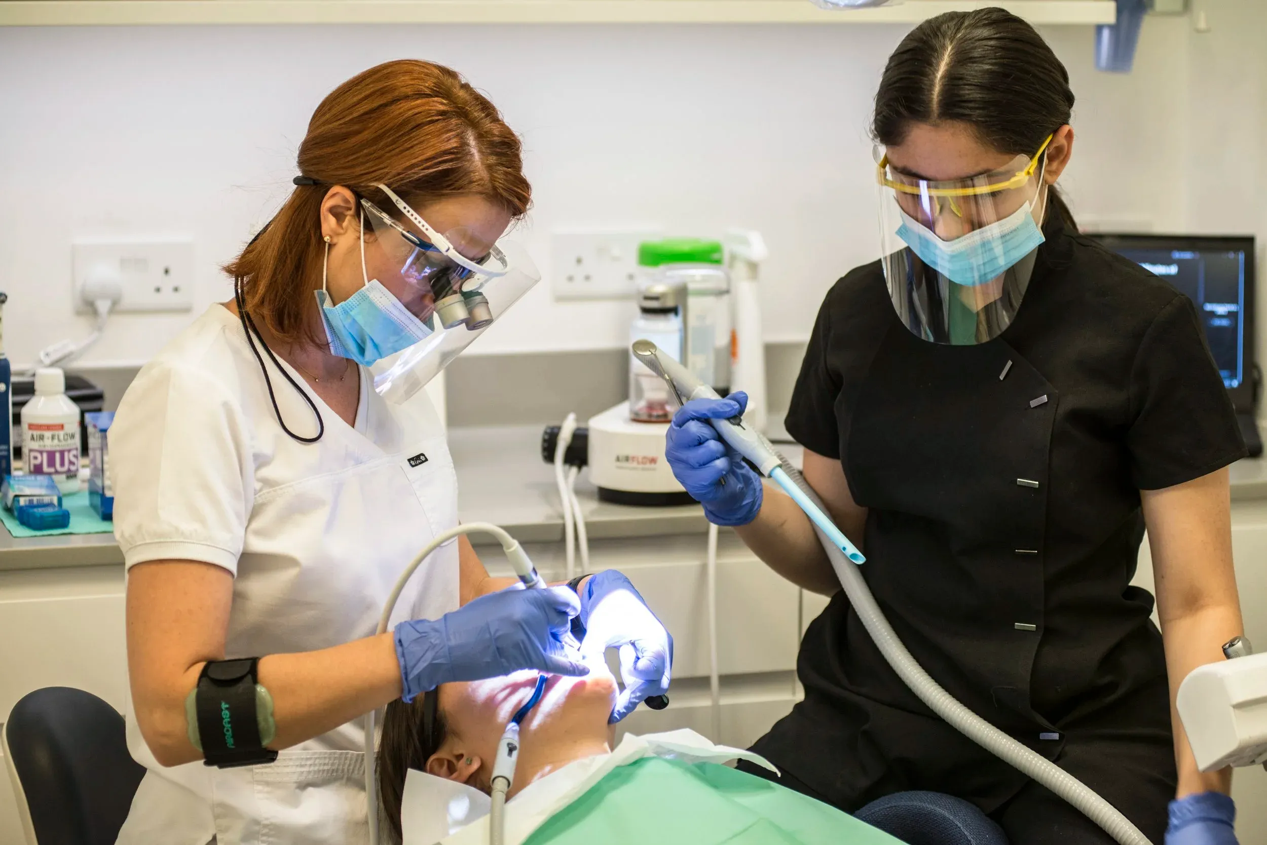 Two dental clinicians in face shields and gloves treating a patient reclined in a dental chair