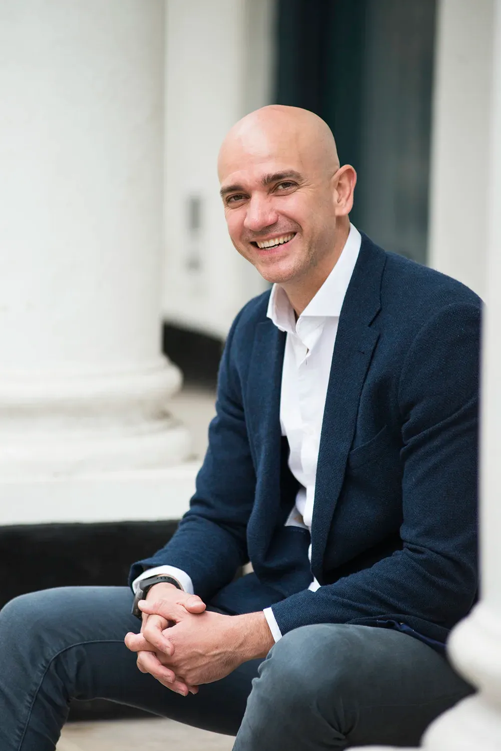 Dr Goran Stojanovic smiling, sitting in a navy blazer and white shirt