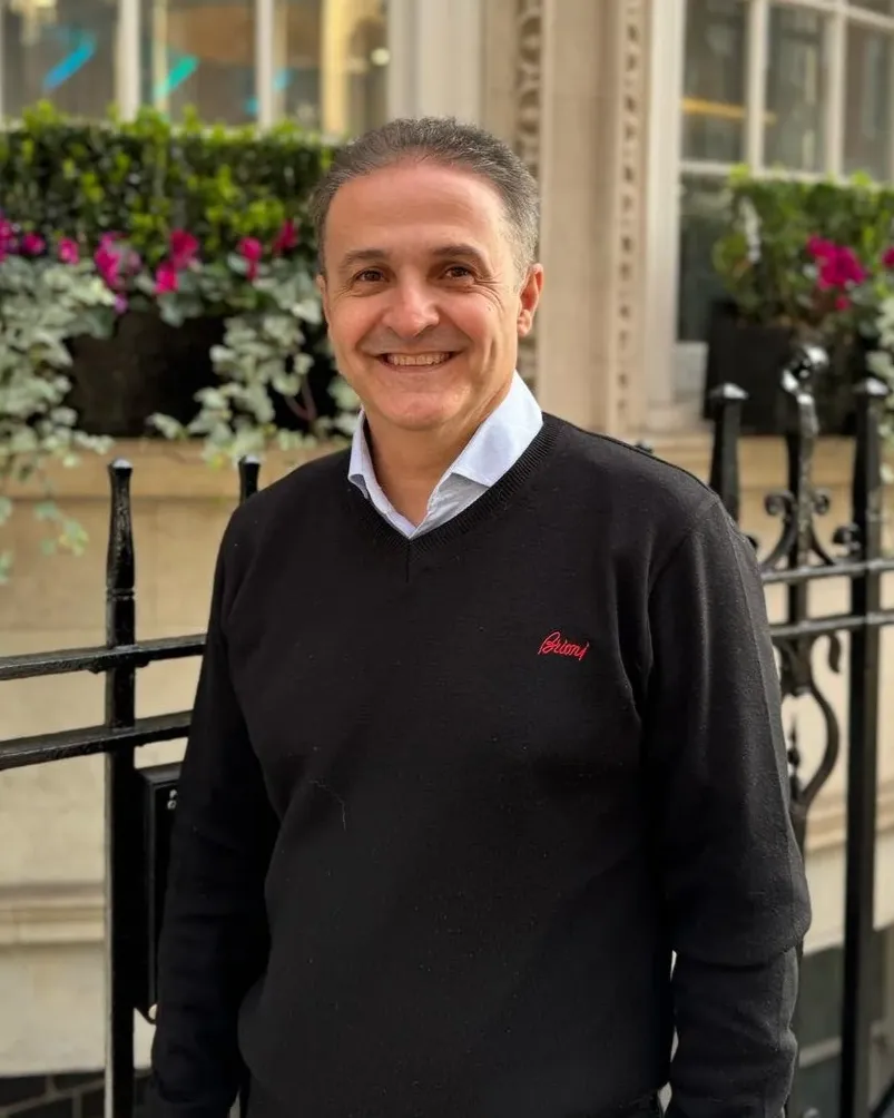 Arash Zaker Shahrak in a black jumper, smiling beside black railings and window boxes