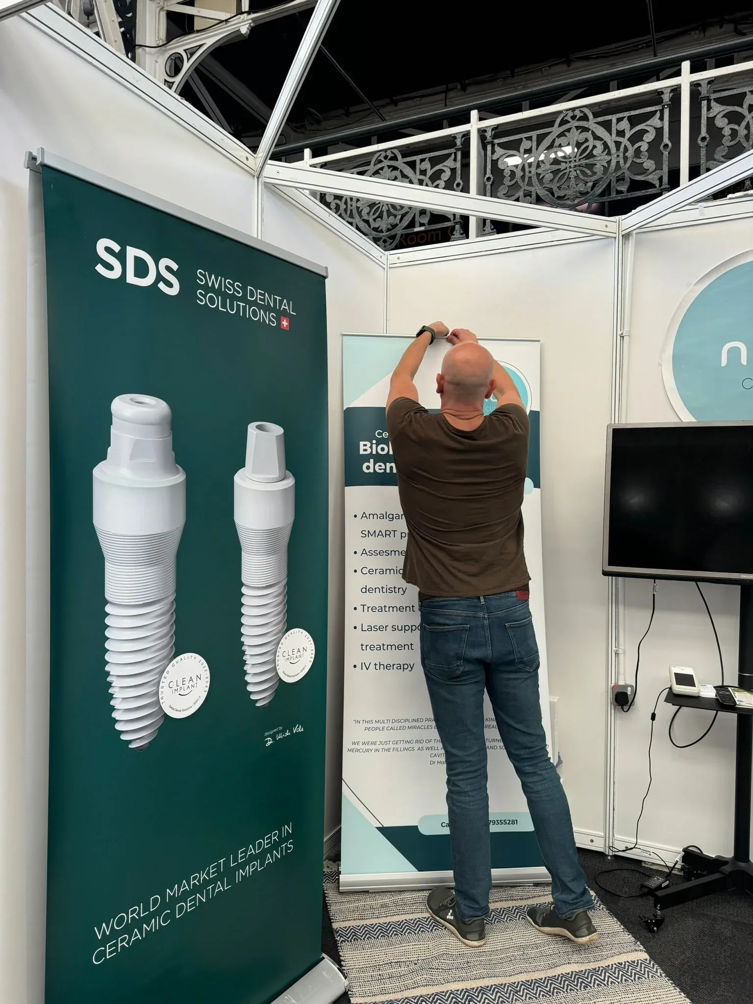 Man putting up a poster on an exhibition stand next to a Swiss Dental Solutions banner