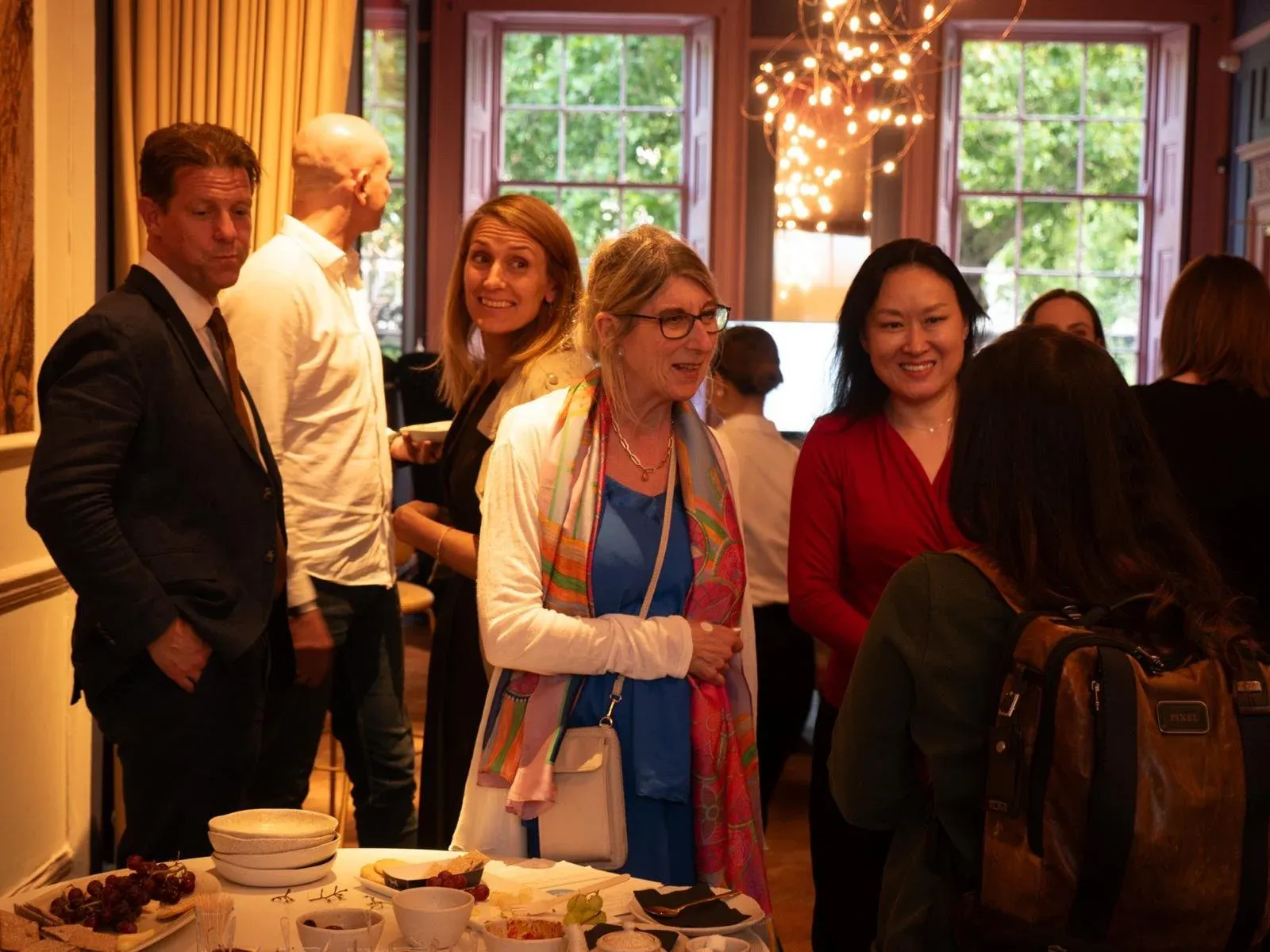 Group of guests chatting beside a table of food in a room with large windows