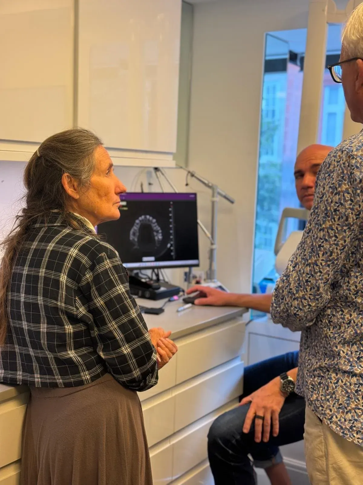 Woman in a checked shirt looking at a dental scan on a monitor, with two men beside her