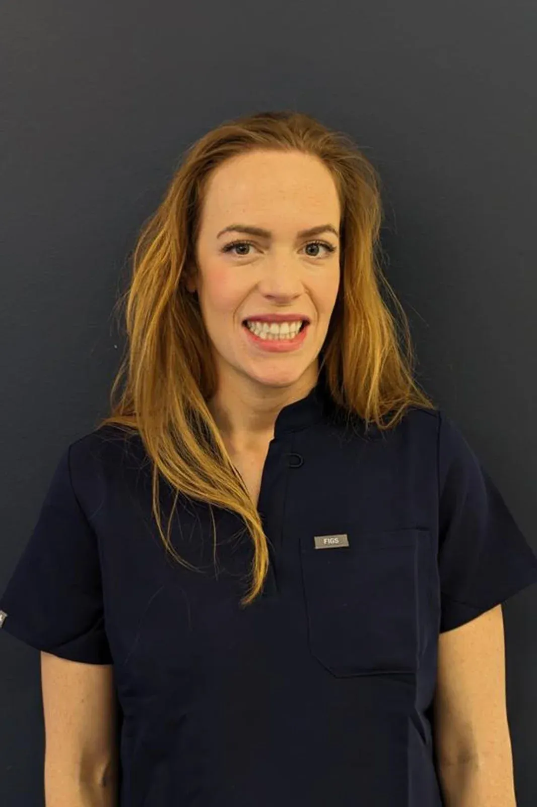 Dr Aoife Stack smiling, in navy scrubs against a dark wall